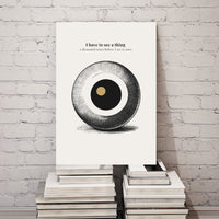 Poster with a circular design and text on a stack of books against a white brick wall.