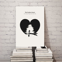 Art print with a black heart silhouette and text on a white background, placed on a stack of books against a white brick wall.