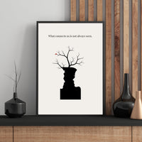 Framed artwork with a black silhouette of a vase with branches and text on a white background, placed on a wooden shelf.