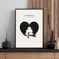 Framed artwork with a black heart design and text on a white background, displayed on a wooden shelf.