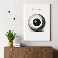 Framed abstract art print on a wall above a wooden cabinet with a plant and books.