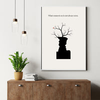Framed artwork with a black silhouette of a person and branches on a white wall above a wooden cabinet.