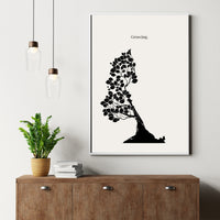 Framed black and white tree art print on a wall above a wooden cabinet with a plant and books.