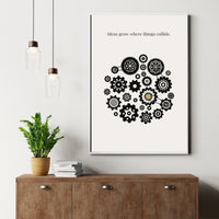 Framed artwork with gears and text on a wall above a wooden cabinet with a plant and books.