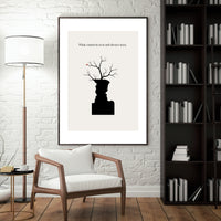 Framed artwork on a wall above a wooden chair in a room with a lamp and bookshelf.