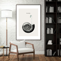 Framed black and white art print on a wall above a wooden chair in a room with a lamp and bookshelf.