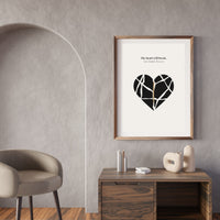 Framed artwork with a black heart design on a gray wall above a wooden desk.