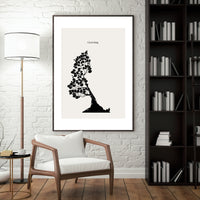 Framed black and white artwork of a tree on a wall in a living room with a chair, lamp, and bookshelf.