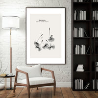 Framed artwork on a wall above a wooden chair in a room with a lamp and bookshelf.