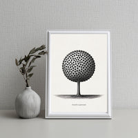 Framed black and white tree art print on a gray wall with a vase containing leaves.