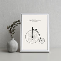 Framed print with bicycle illustration and quote on a textured wall with a vase.