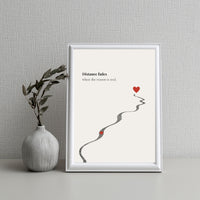 Framed artwork with a heart and path on a gray wall with a vase.