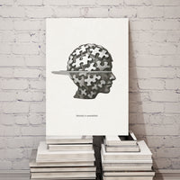 Canvas print with a puzzle piece design on a head, placed on books against a white brick wall.
