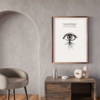 Framed artwork with an eye illustration and text on a wall above a wooden desk.
