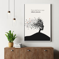 Poster with a black and white silhouette of a person with leaves, placed above a wooden cabinet with a plant and books.