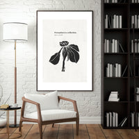 Framed artwork with a black and white design on a wall in a room with a chair, lamp, and bookshelf.