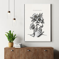 Framed artwork of a hand holding flowers on a wall above a wooden cabinet with a plant and books.
