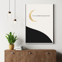Framed artwork with a gold crescent moon and text on a white wall above a wooden cabinet.