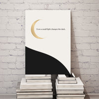 Canvas print with a gold crescent moon and text on a stack of books against a white brick wall.