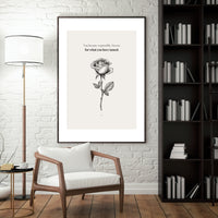 Framed artwork with a rose and text in a room with a chair, lamp, and bookshelf.