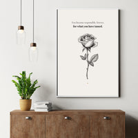 Framed artwork with a rose illustration and text on a wall above a wooden cabinet.